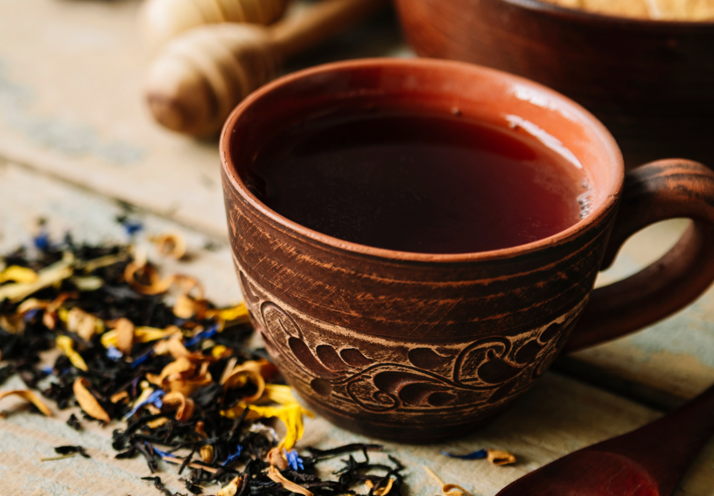 Copo de chá com colher de madeira e ervas em volta.