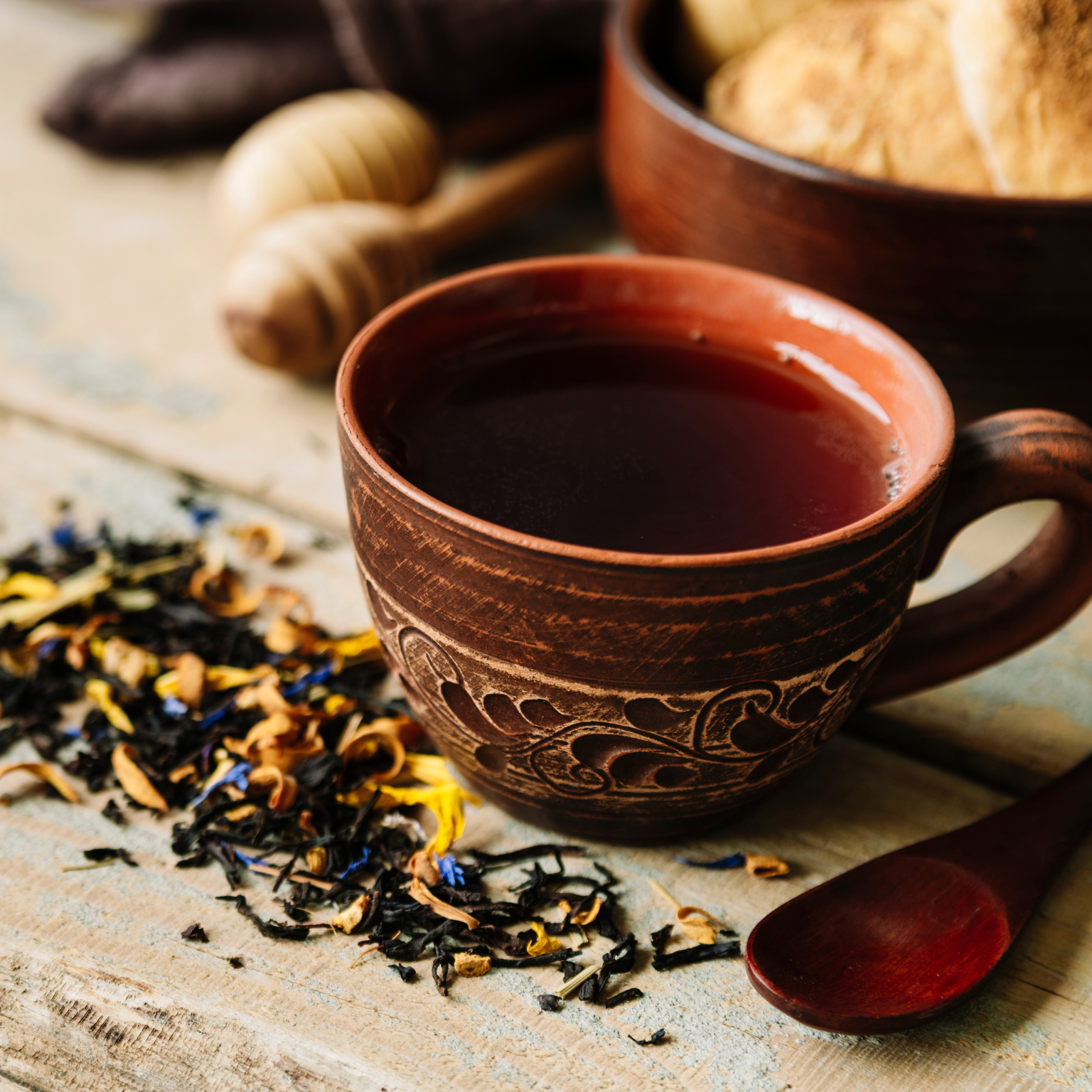 Copo de chá com colher de madeira e ervas em volta.